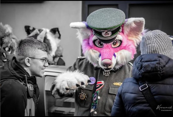 Ч/б фото: два фурсьюта в немецкой военной форме (один в длинной шинели, второй в кителе с Железным крестом) стоят на городской улице перед торговым центром (10/21).