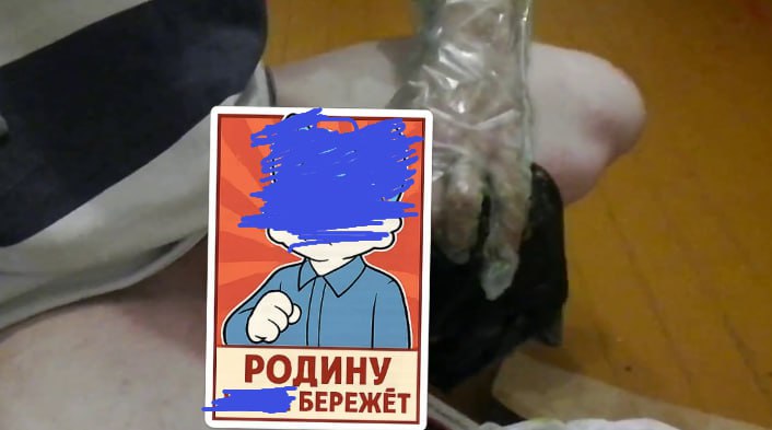 Рука держит советско-стилизованный стикер «РОДИНУ [синяя цензура] БЕРЕЖЁТ» на фоне упакованной чёрной интимной игрушки.