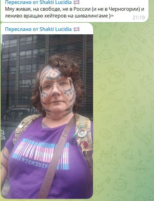 Скриншот из чата: сообщение от Shakti Lucidia — фото женщины с леопардовыми татуировками на лице, в фиолетовой футболке с надписью TRANSGENDER (зеркально). Подпись: «Мяу живая, на свободе, не в России (и не в Черногории) и лениво вращаю хейтеров на шивалингаме».