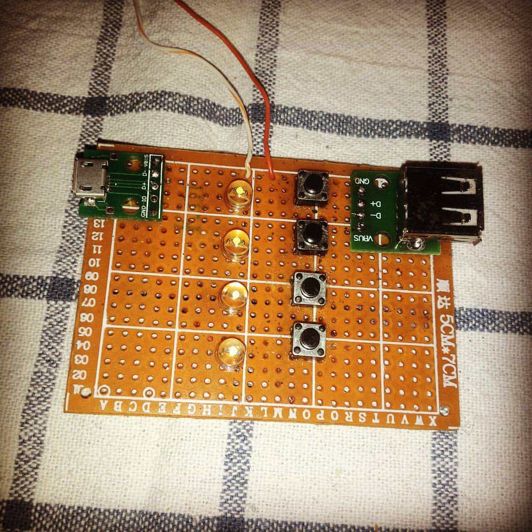 DIY-плата на оранжевой текстолитовой макетке (перфорированной): слева — разъём micro-USB, по центру — четыре тактовые кнопки в ряд, справа — разъём USB-A и небольшой модуль; соединения выполнены проводами; плата лежит на клетчатой ткани
