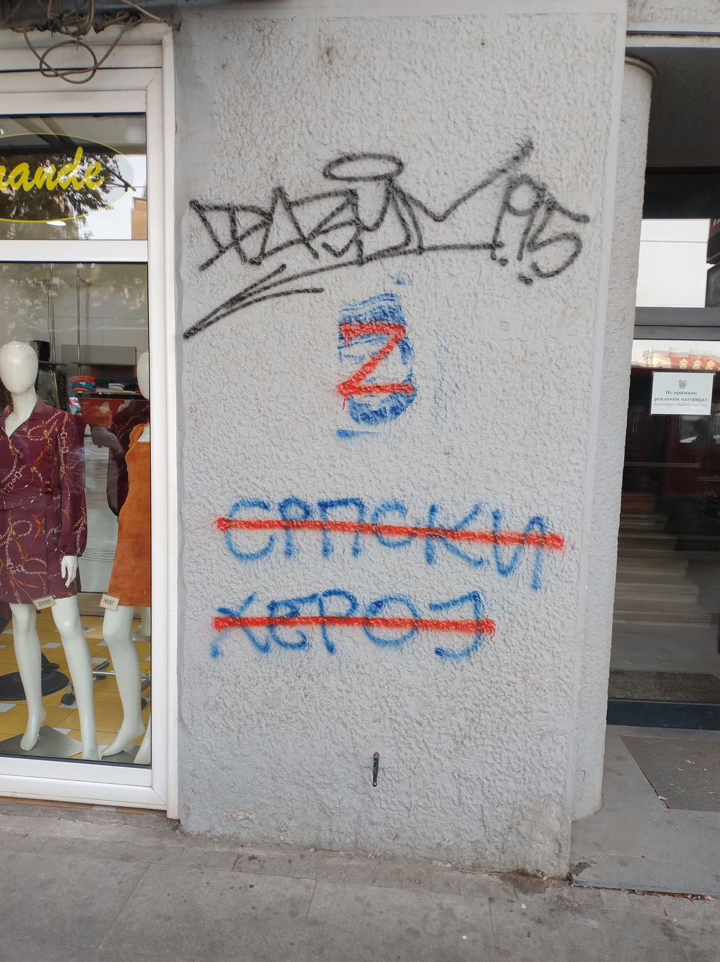 📷 Граффити на углу стены здания: символ Z синего цвета, ниже слово «Српски» синим — зачёркнуто красной горизонтальной чертой, ниже слово «Херој» — также зачёркнуто красным; рядом теги.