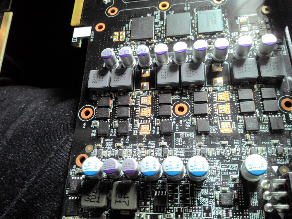 Крупный план PCB видеокарты: ряды фиолетовых и синих конденсаторов, дроссели, транзисторы VRM-зоны питания; маркировки компонентов
