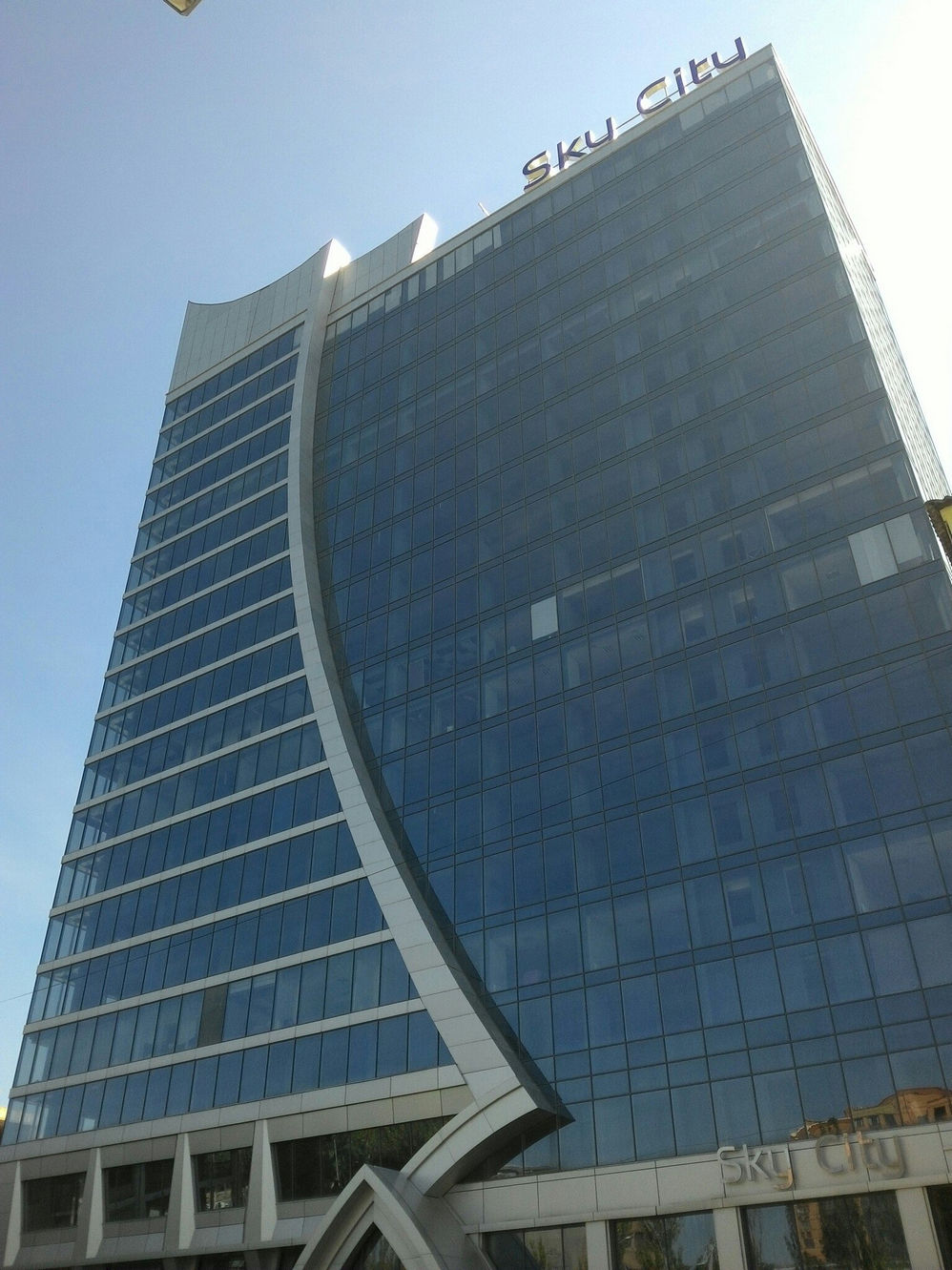 Небоскрёб «Sky City» в Донецке: высотное здание с изогнутым стеклянным фасадом и логотипом «Sky City» на крыше; снято снизу вверх против солнечного неба