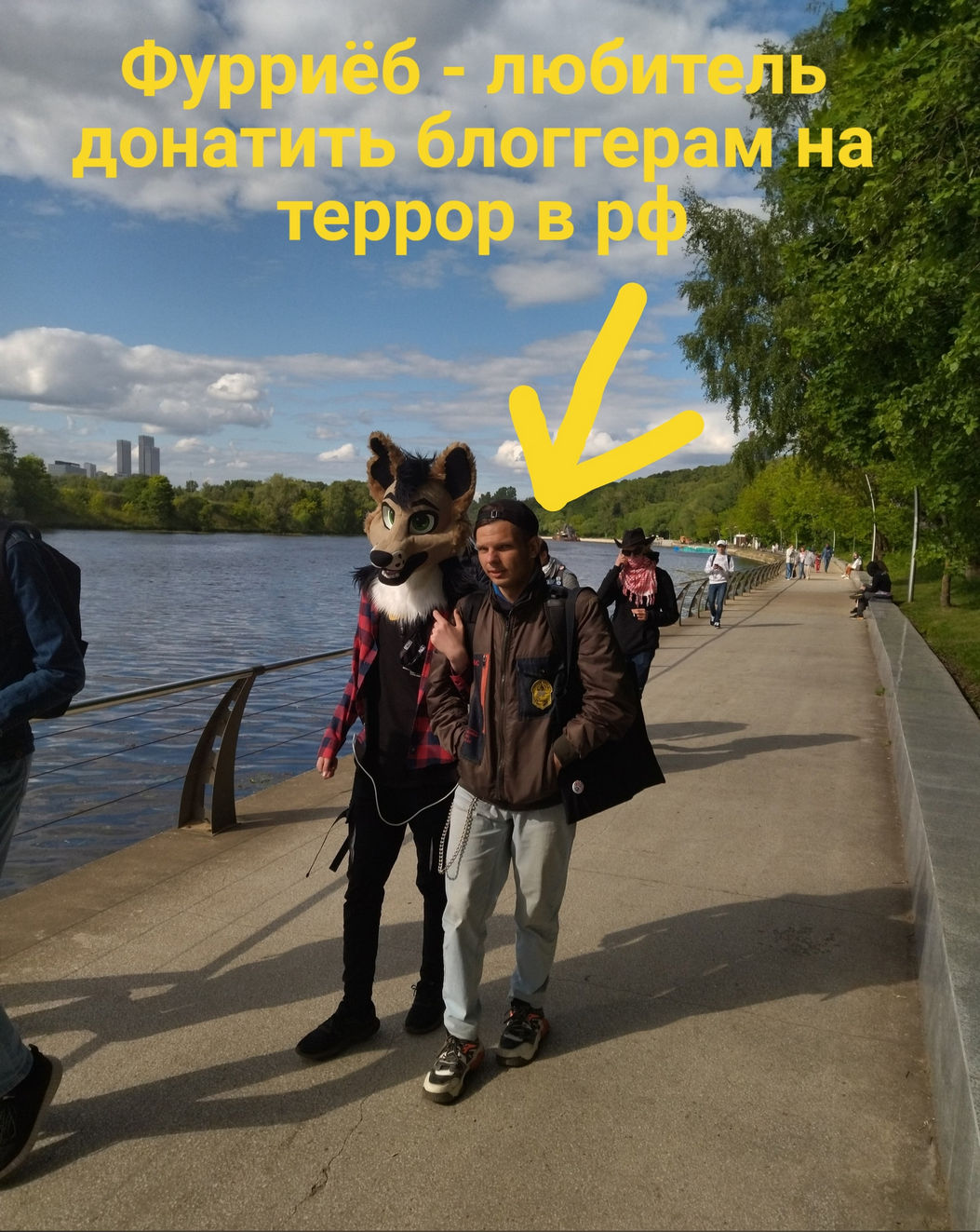 🖼️ Набережная реки; стоят двое — мужчина с надетой головой коричневого фурсьюта и человек рядом; жёлтая стрелка вниз и надпись «Фурриёб — любитель донатить блоггерам на террор в рф».