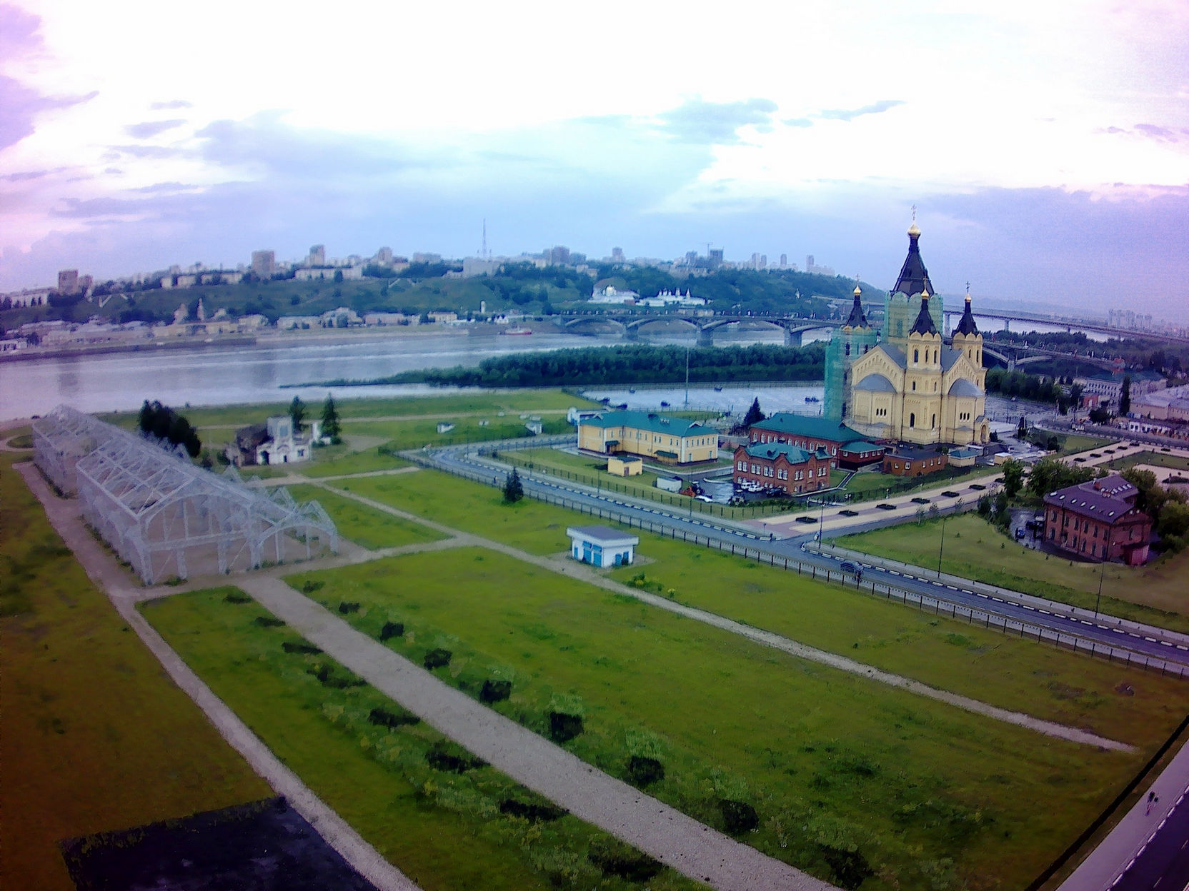 📷 Аэросъёмка Нижнего Новгорода: зелёная пойма, Александро-Невский собор с золотыми куполами справа, слияние Оки и Волги слева, мост и городская застройка на холмах вдали