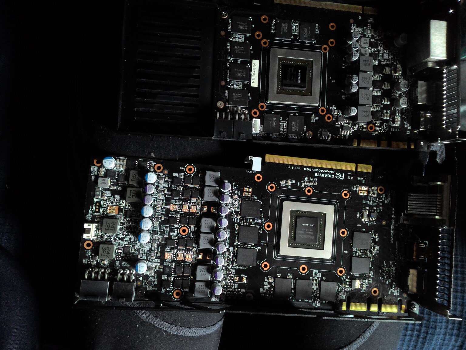Две видеокарты без систем охлаждения (голые PCB): нижняя — Gigabyte GP-R7850C-2GD Rev 2.0 (AMD Radeon HD 7850), верхняя — аналогичная; оранжевые крепёжные кольца, конденсаторы, разъёмы питания