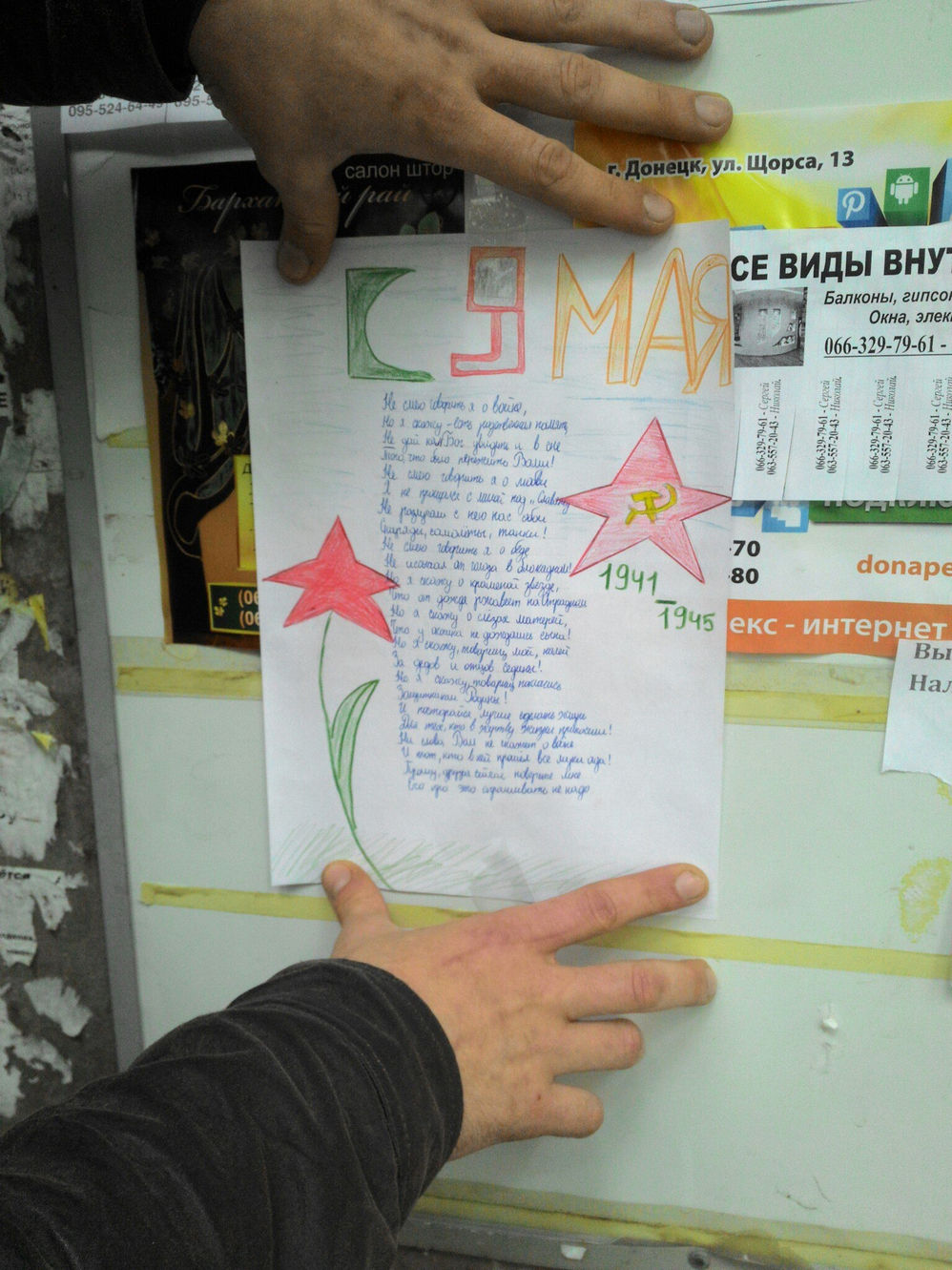 Листовка ко Дню Победы, прикреплённая скотчем к доске объявлений в Донецке (ул. Щорса, 13): надпись «9 МАЯ», рисунок тюльпана и красной звезды с серпом и молотом, годы 1941–1945; рукой прикреплён листок