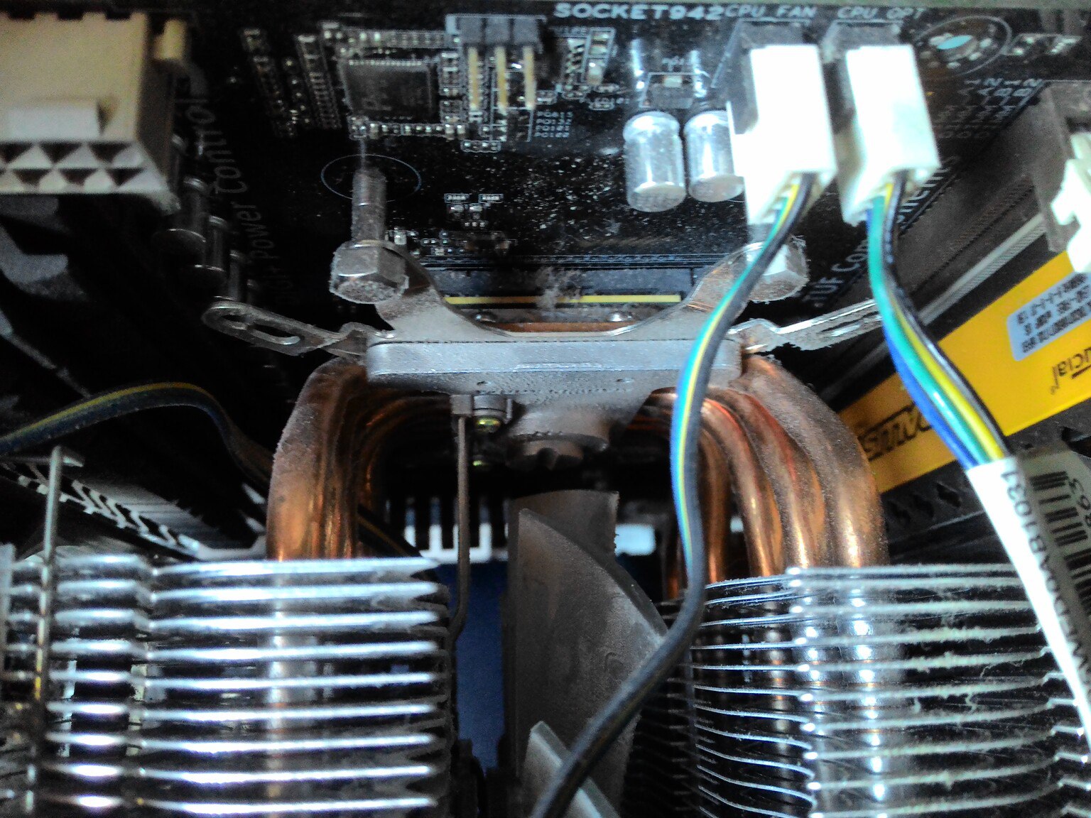 Крупный план кулера CPU на материнской плате: медные тепловые трубки огибают алюминиевые рёбра радиатора; на плате надписи SOCKET942, CPU FAN, CPU OPT; жёлто-синие провода