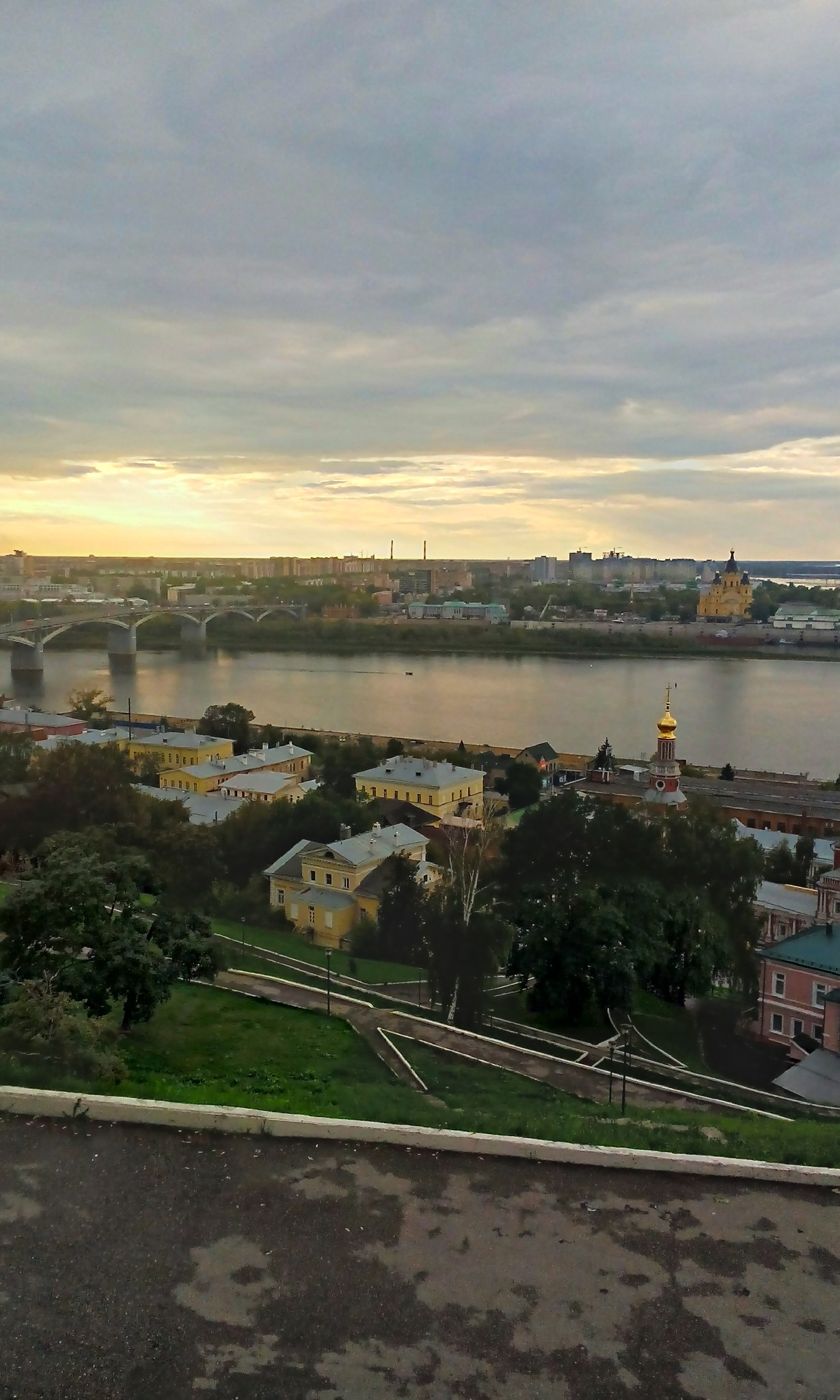 Вид с высоты на Нижний Новгород: Ока, Канавинский мост, исторические здания Нижегородского посада, церковь с золотым куполом; вечернее небо с облаками