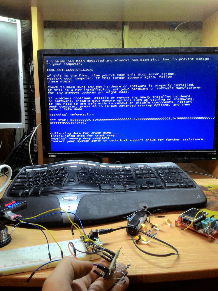 Фото монитора с синим экраном смерти (BSOD, Blue Screen of Death): белый текст на синем фоне с сообщением об ошибке Windows; перед монитором эргономичная клавиатура; на столе Arduino-совместимые платы и электронные компоненты