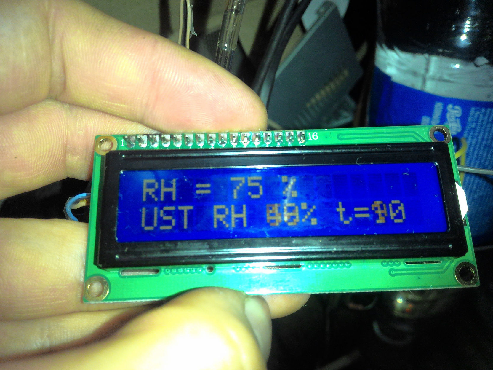 Фото в руке синего LCD-дисплея 16×2: на экране две строки — «RH = 75 %» и «UST RH 40% t=90» (показание датчика влажности и уставки регулятора)
