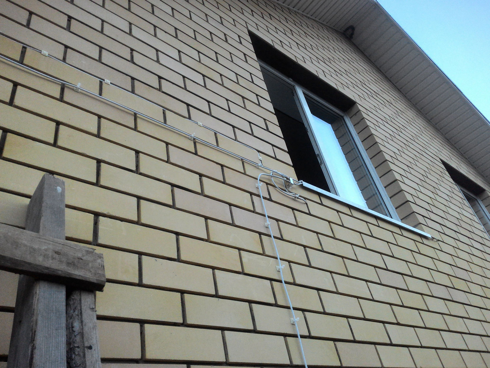 Фото кирпичного фасада здания (жёлтый кирпич): антенный кабель проложен вертикально по стене вниз на металлических скобах; рядом окно