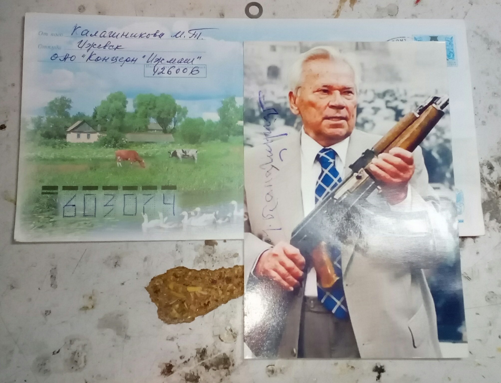 На рабочем столе: конверт с обратным адресом «Калашникова М.Т., Ижевск, ОАО Концерн Ижмаш» и рядом фотография пожилого Калашникова с АКМ в руках с синей подписью-автографом