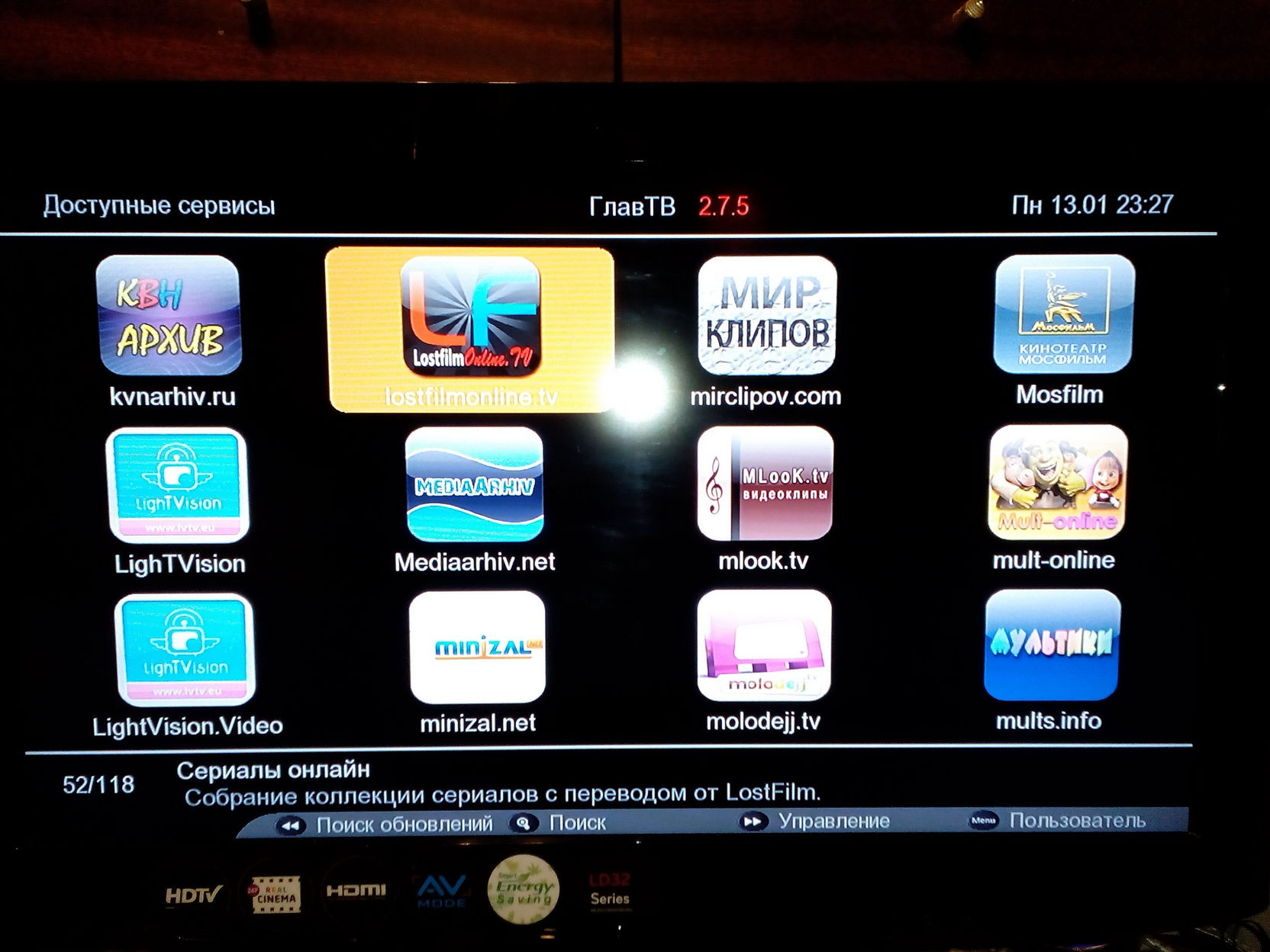 Экран телевизора: IPTV-приложение ГлавТВ 2.7.5, раздел «Доступные сервисы» со списком каналов — КВН Архив, LostFilm, Мир Клипов, Мосфильм и другие; дата 13.01 23:27