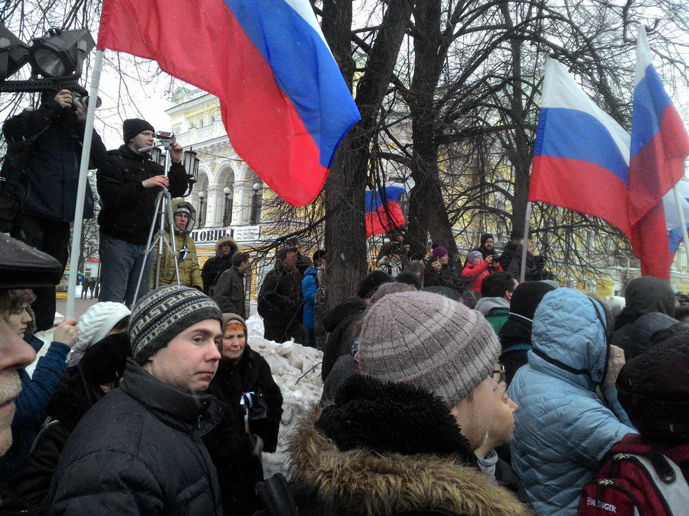 Фото митинга: участники с российскими флагами стоят у деревьев, кто-то выступает с возвышения; зима, серое небо