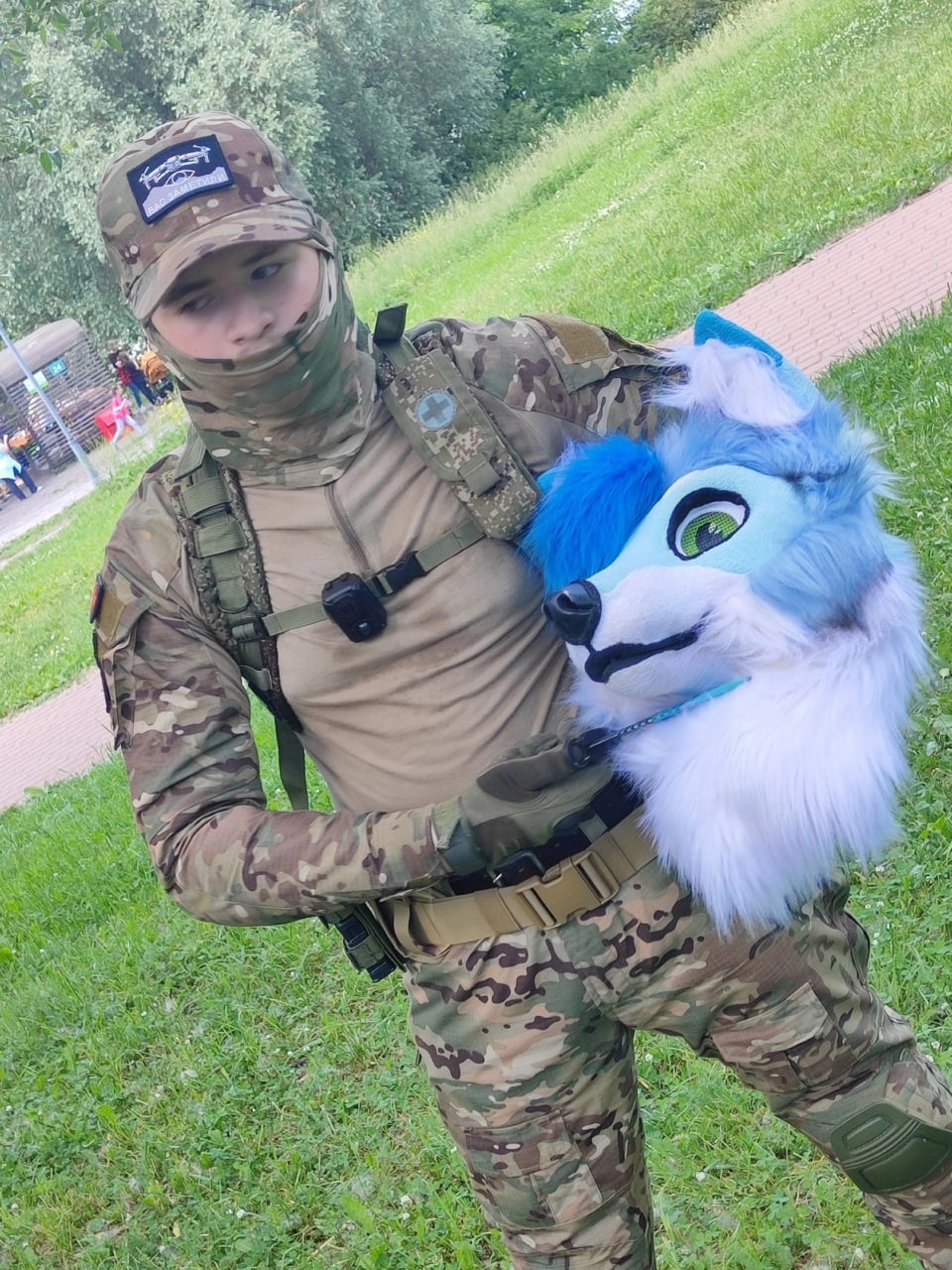 📷 Человек в военной форме держит синюю фурри-голову волка с голубыми глазами.