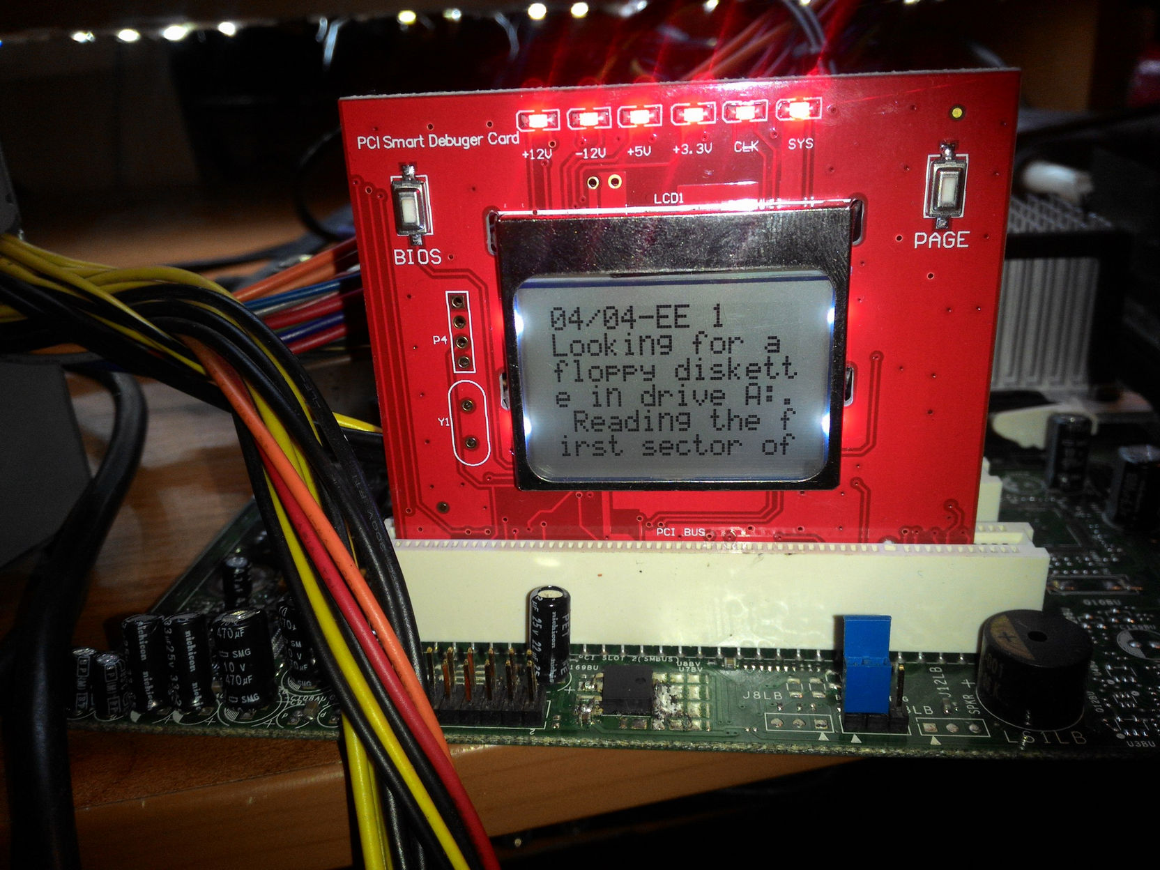 Красная отладочная карта PCI Smart Debugger Card установлена в слот материнской платы: ЖК-экран отображает код «04/04-EE 1» и сообщение «Looking for a floppy diskette in drive A: Reading the first sector of»; индикаторы напряжений +12V, -12V, +5V, +3.3V, CLK, SYS горят