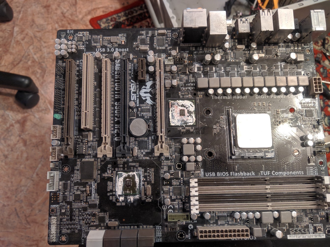 Материнская плата ASUS ATX на столе: надписи «Thermal Armor», «USB BIOS Flashback», «1TV Components»; сокет AM3+, слоты PCI-E, разъёмы питания