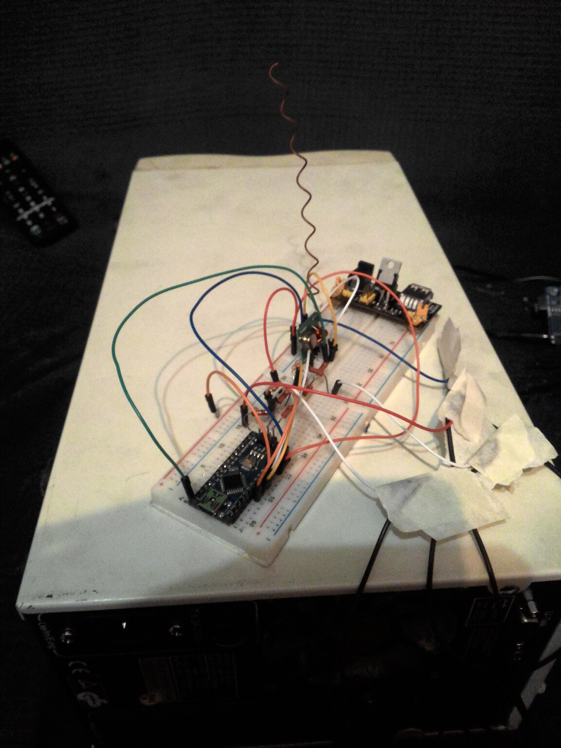 Фото сверху: макетная плата на белом картоне — Arduino Nano (или аналог), блок питания, разноцветные провода (зелёные, красные), компоненты; на чёрном фоне
