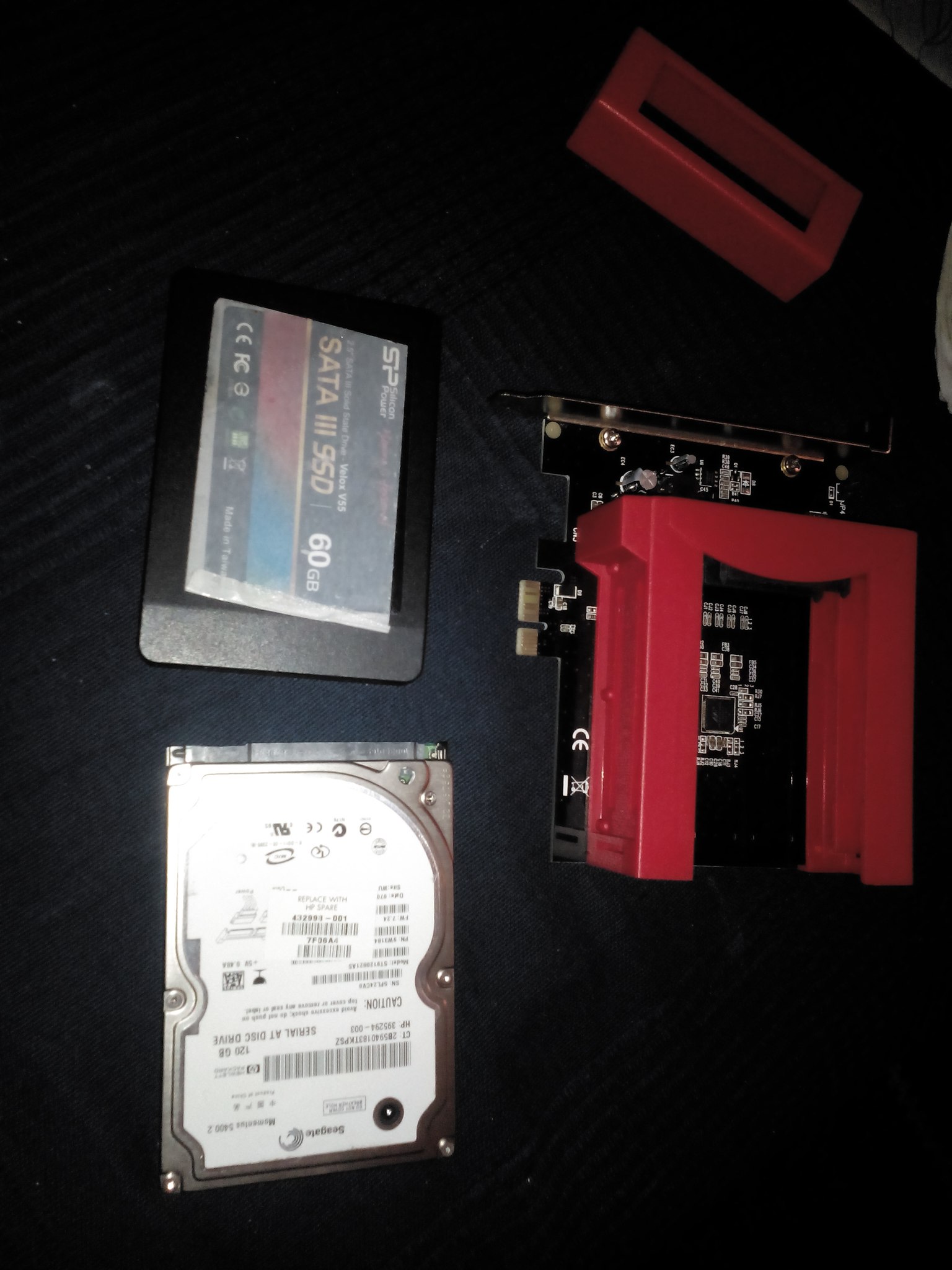 Silicon Power SATA III SSD 60 ГБ (Velox V55) и Seagate Momentus 5400.2 HDD 120 ГБ, разложены на чёрной ткани рядом с красным PCIe-адаптером