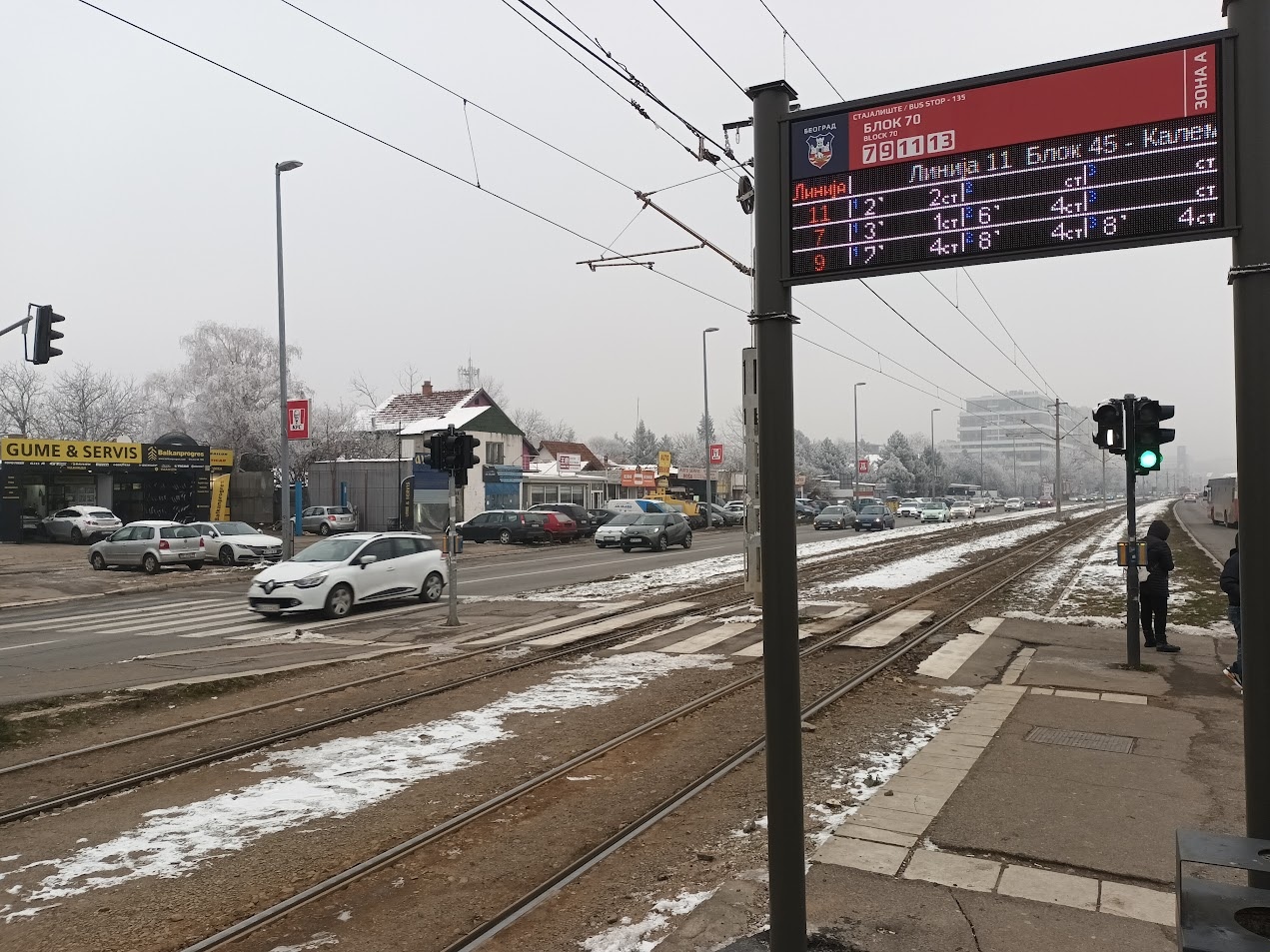 📷 Трамвайная остановка: электронное табло маршрутов (маршрут 13 Блок 45 — Калемегдан; маршруты 1, 3 с временами прибытия); трамвайные пути, автомобили, заснеженные деревья на фоне.