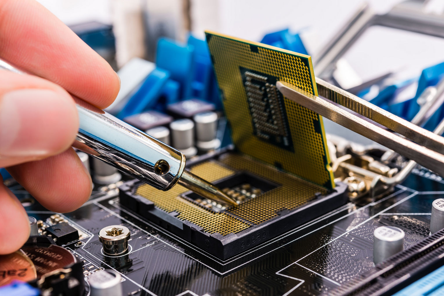 📷 Крупный план: руки держат пинцетом золотой CPU и опускают его в синюю материнскую плату; конденсаторы и компоненты платы вокруг.