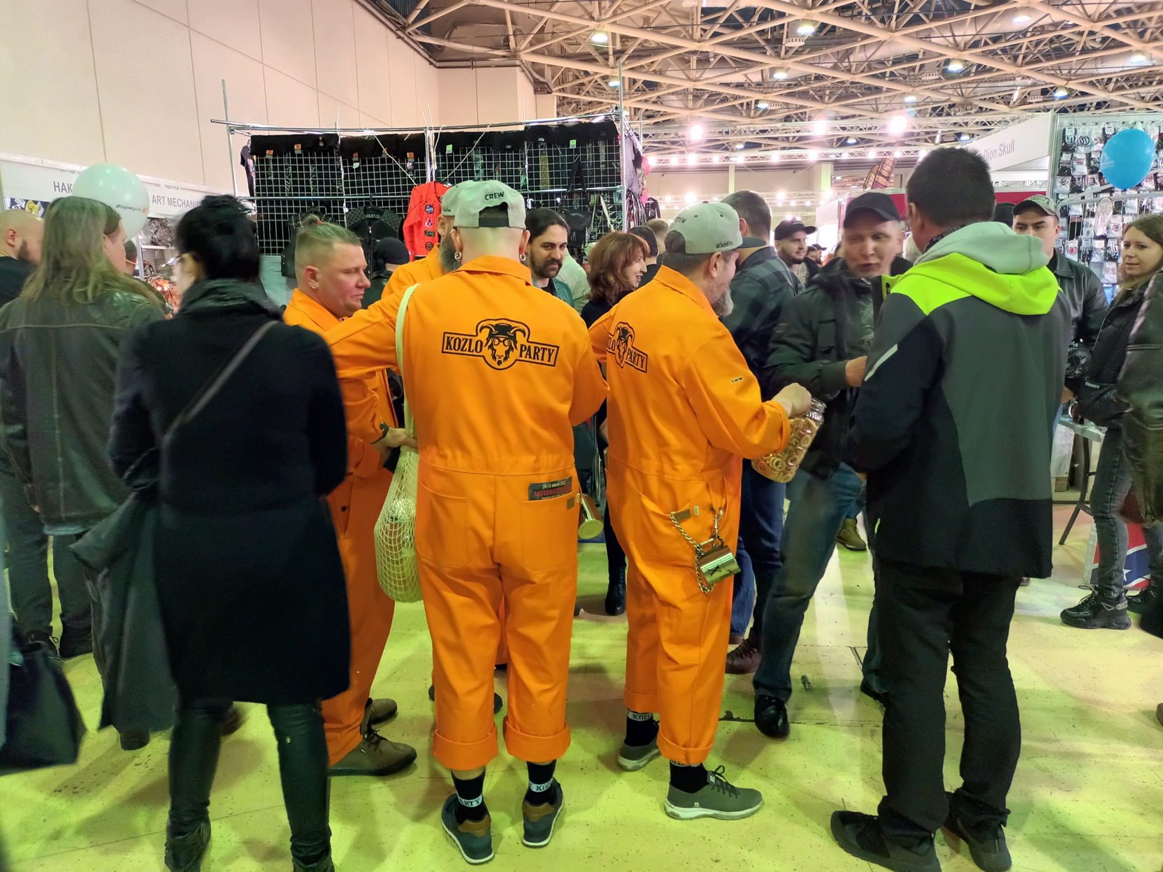 📷 Выставка: группа людей в ярко-оранжевых комбинезонах с логотипом «WOLF...» на спине стоит в кружке среди посетителей.