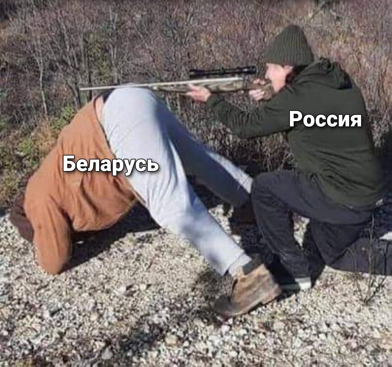 🖼️ Мем. Фото двух мужчин на каменистой местности: один (подпись «Беларусь») стоит на коленях и пригнулся, другой (подпись «Россия») стоит и прижимает его голову ружьём.
