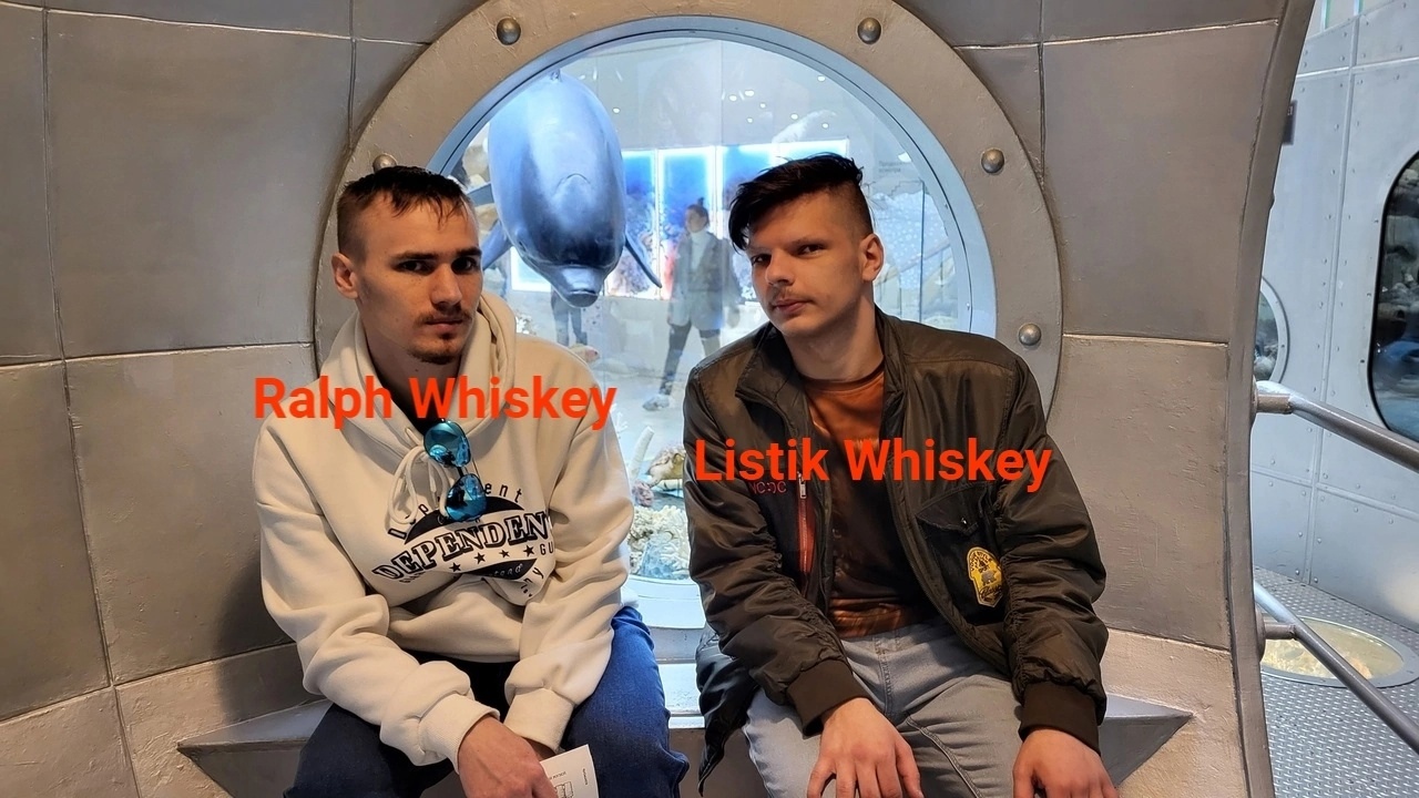 📷 Фото двух молодых людей, сидящих в цилиндрическом модуле музея: слева «Ralph Whiskey» (белый худи), справа «Listik Whiskey» (куртка-бомбер); фон — музейная экспозиция с макетами.