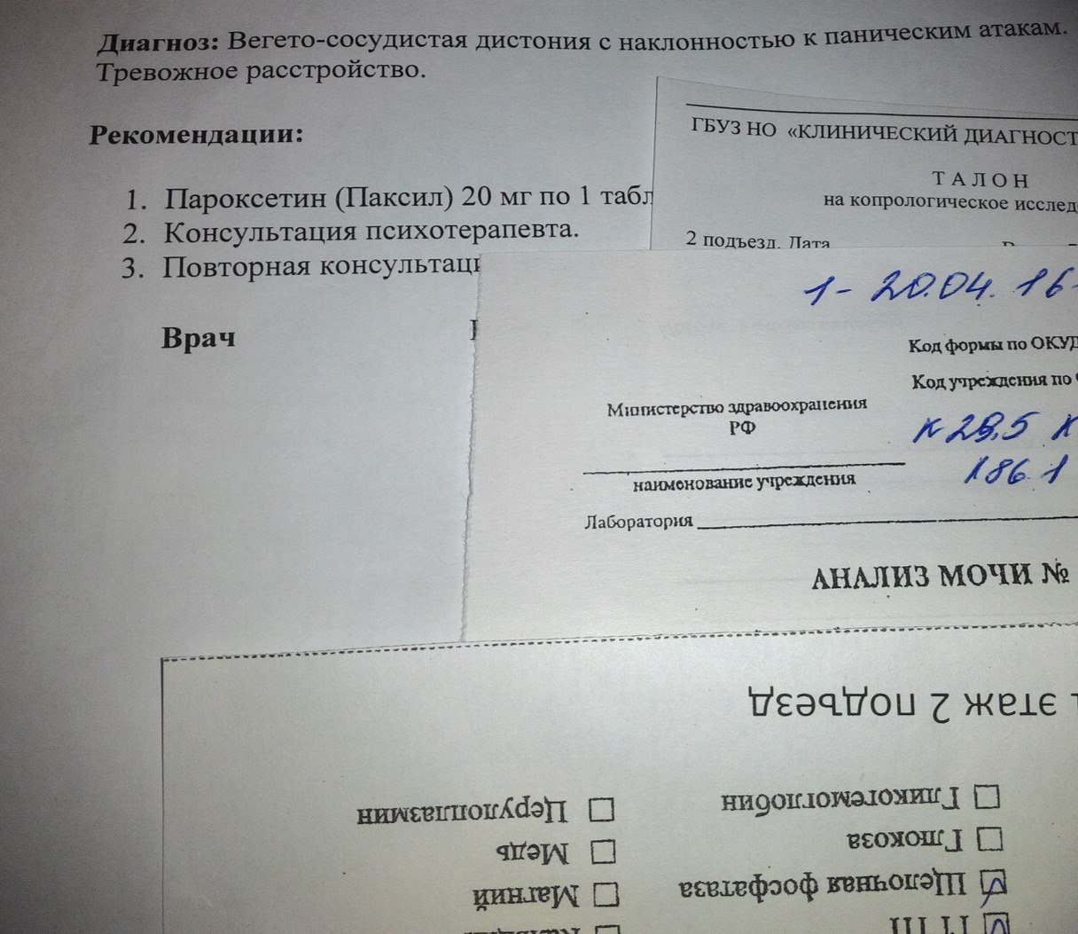 Фото двух медицинских документов, наложенных друг на друга: верхний — «Диагноз: Вегето-сосудистая дистония с наклонностью к паническим атакам. Тревожное расстройство. Рекомендации: 1. Пароксетин (Паксил) 20 мг по 1 табл... 2. Консультация психотерапевта. 3. Повторная консультация... Врач»; справа видно «ГБУЗ НО «КЛИНИЧЕСКИЙ ДИАГНОС...»; «ТАЛОН на копрологическое исслед...»; «2 подъезд. Пята»; «1- 22О4 16»; «Министерство здравоохранения РФ»; «АНАЛИЗ МОЧИ №»; нижний документ перевёрнут — виден бланк анализа мочи с чекбоксами (Гликогемоглобин, Глюкоза, Щелочная фосфатаза, Церулоплазмин, Медь, Магний)
