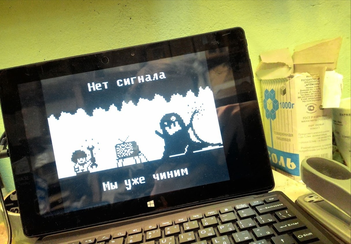 📷 Планшет с клавиатурой на столе; на экране — чёрно-белая игра/программа с надписями «Нет сигнала» и «Мы уже чиним», схематичные персонажи. На заднем плане флакон соли.