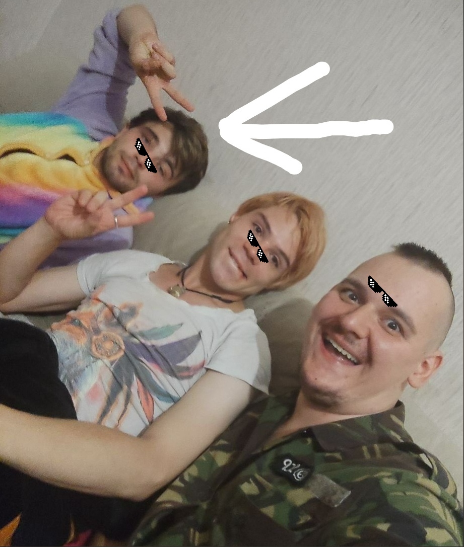 📷 Групповое селфи трёх молодых людей у светлой стены: слева в радужной кофте с жестом «коза», в центре со светло-рыжими волосами в белой футболке, справа лысый в камуфляжной куртке; на всех пиксельные очки; белая стрелка указывает на левого.