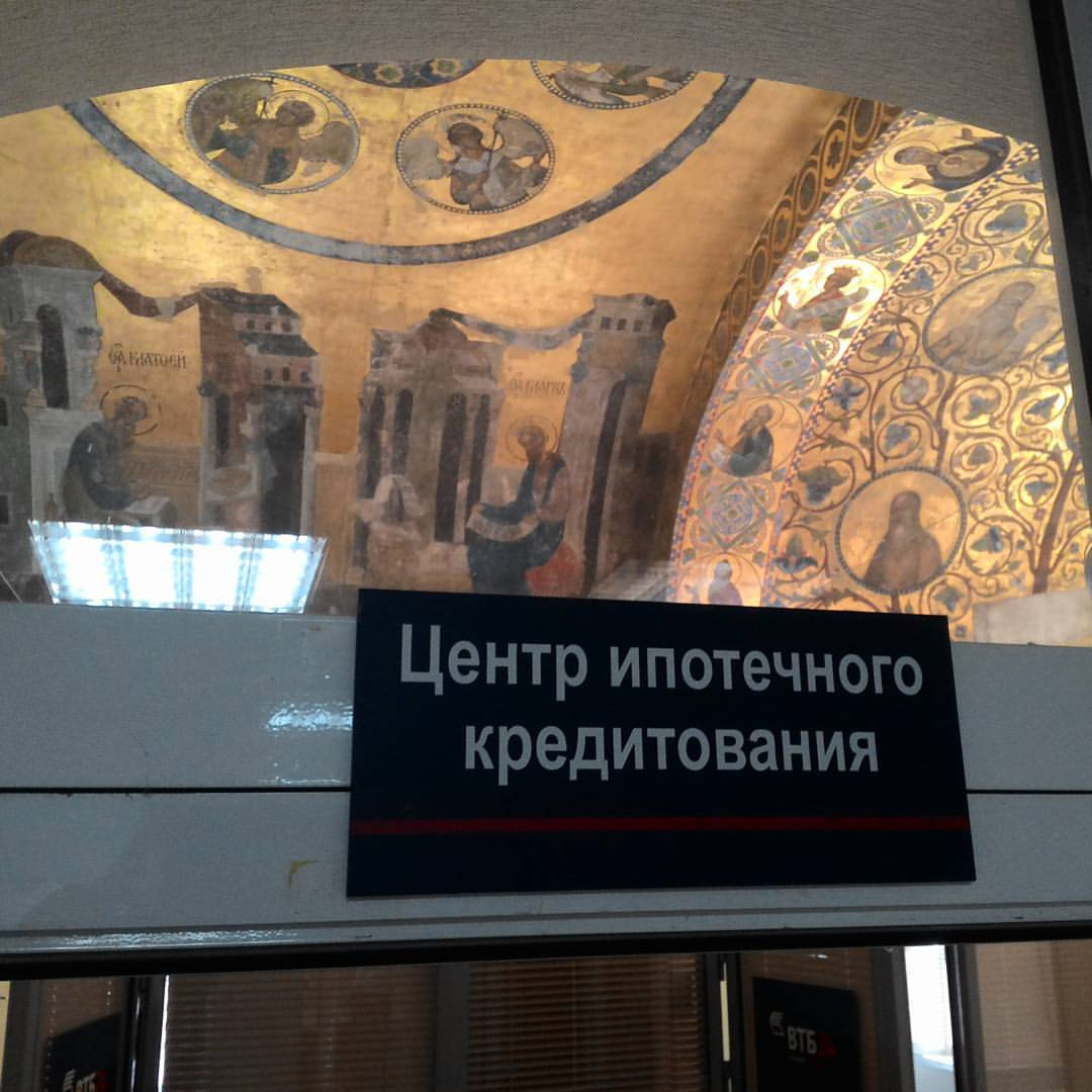 Фото: на переднем плане — табличка «Центр ипотечного кредитования» на стеклянной двери/перегородке; на заднем плане — сводчатый потолок с золотыми православными мозаиками и фресками с изображением святых