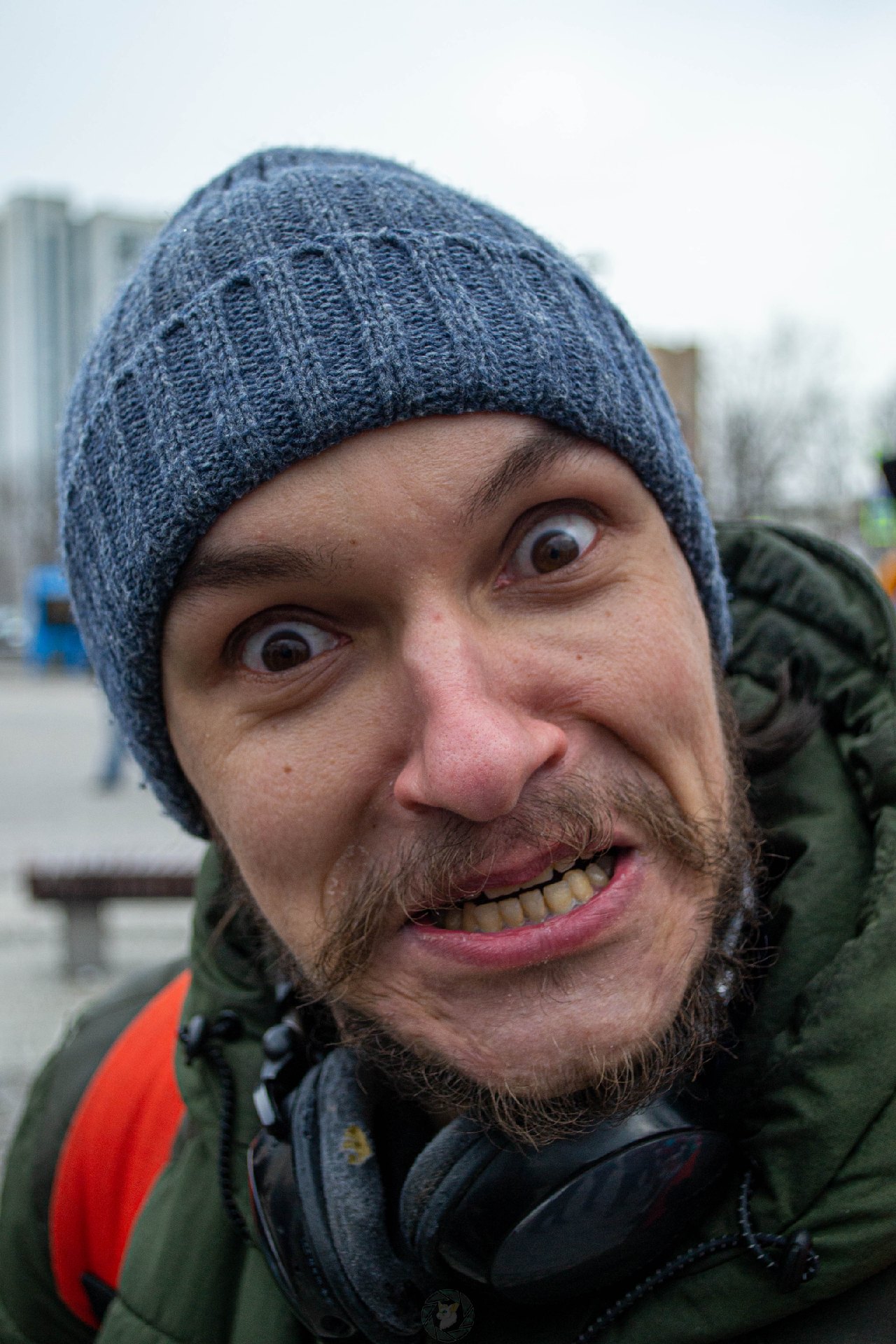📷 Крупный план лица мужчины в тёмной шапке на фоне городских зданий.