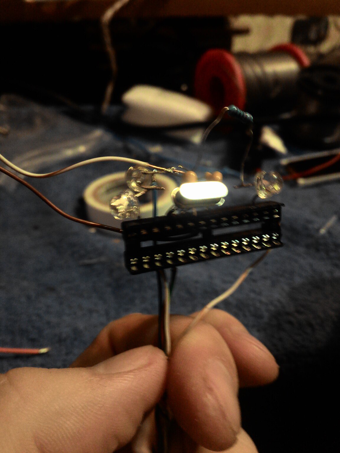 Фото руки, держащей маленькую Arduino-совместимую плату (Pro Mini или аналог): горит белый светодиод, в нижнем торце установлен DIP-28 разъём; на заднем плане синяя ткань и красный цилиндрический объект