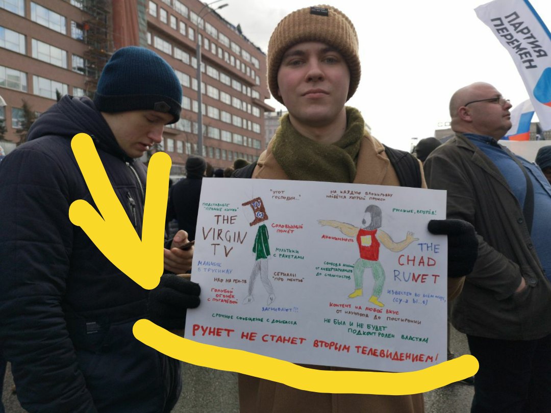 Митинг против изоляции рунета: молодой человек в бежевой шапке держит белый плакат с мемом-рисунком «THE VIRGIN TV» (сутулая фигурка с описанием телевидения) и «THE CHAD RUNET» (уверенная фигурка); снизу надпись «РУНЕТ НЕ СТАНЕТ ВТОРЫМ ТЕЛЕВИДЕНИЕМ!»; жёлтые стрелка и линия подчёркивают плакат; справа видно баннер «ПАРТИЯ ПЕРЕМЕН»