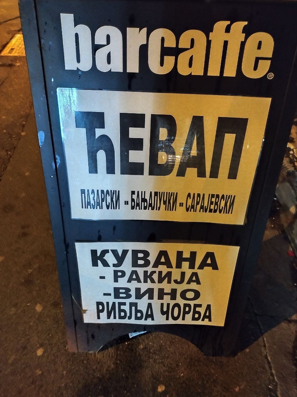 📷 Ночное фото уличной вывески кафе «barcaffe» — «ЋЕВАП ПАЗАРСКИ — БАЊАЛУЧКИ — САРАЈЕВСКИ» и «КУВАНА — РАКИЈА — ВИНО — РИБЉА ЧОРБА» — тёмный фон, мокрый тротуар.
