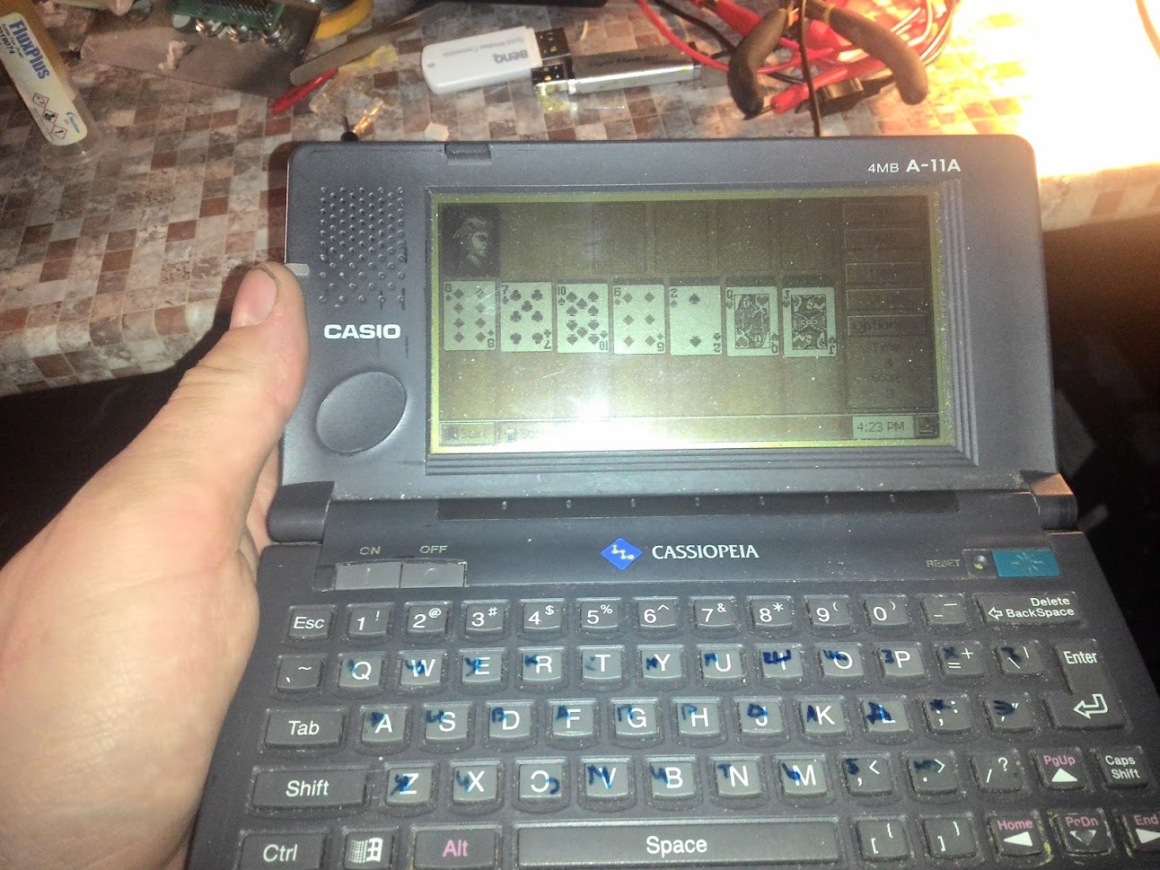 📷 В руке карманный компьютер Casio Cassiopeia (КПК конца 90-х). На пиксельном экране — пасьянс «Косынка». Видна полная QWERTY-клавиатура устройства.