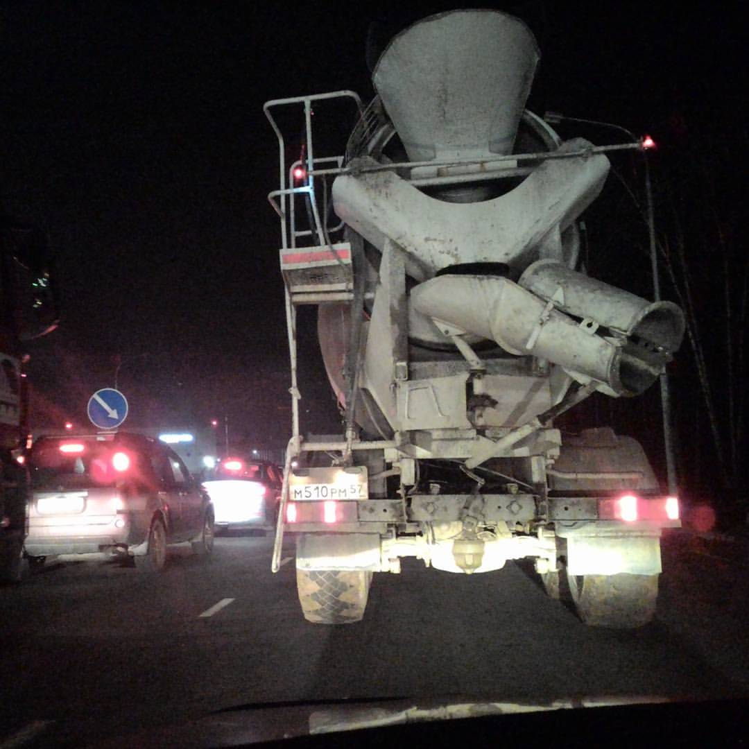 Ночная пробка на московской дороге: вид из салона автомобиля — прямо впереди серая бетономешалка с государственным номером «М510РМ 97»; слева — синий дорожный знак с белыми стрелками-направлениями; на заднем плане — красные огни тормозов других машин; ночь