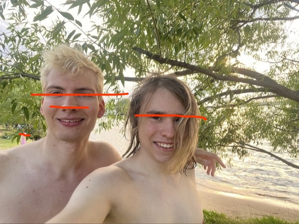 📷 Двое молодых людей (без рубашек, ~16–20 лет) обнимаются и снимают селфи; берег реки, деревья; лица скрыты горизонтальными оранжевыми полосами.
