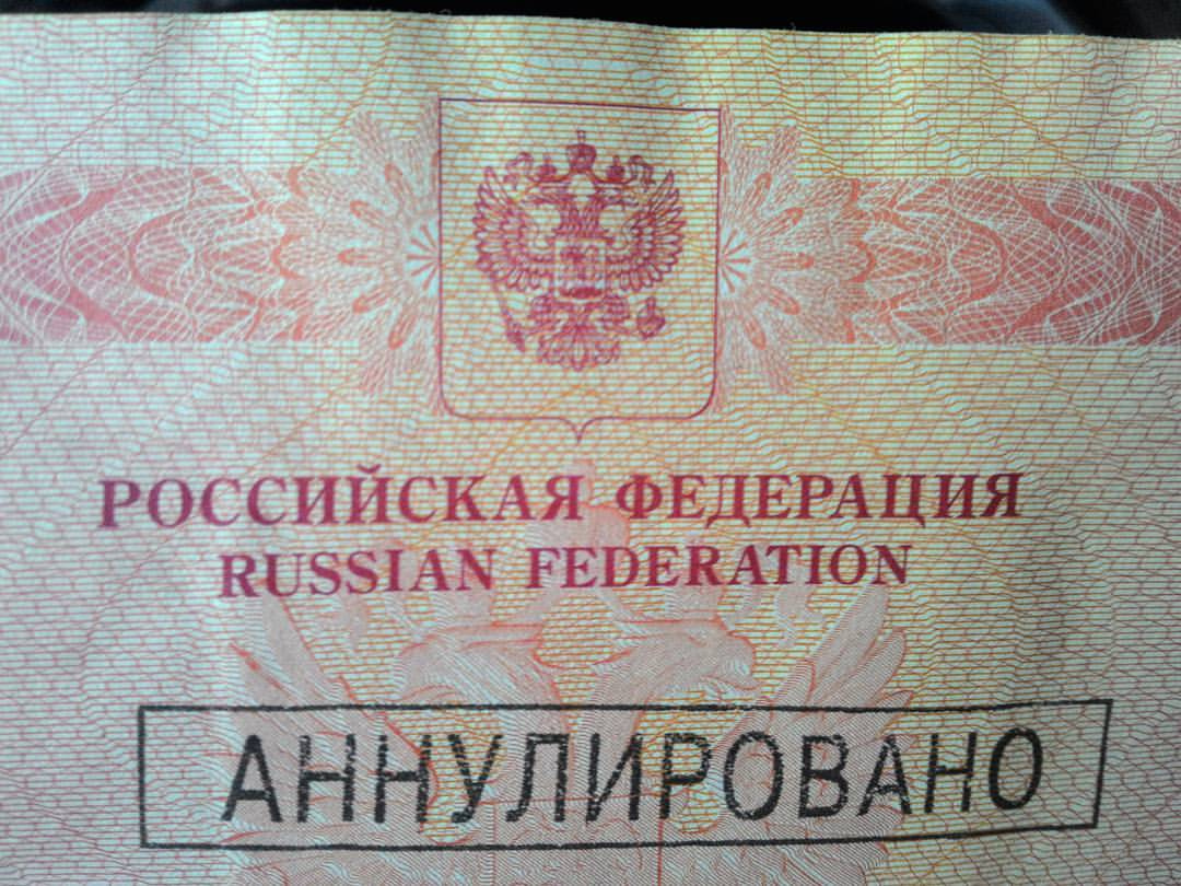 Крупный план страницы российского паспорта: гильошированный розовый защитный фон; вверху — герб Российской Федерации и надписи «РОССИЙСКАЯ ФЕДЕРАЦИЯ» / «RUSSIAN FEDERATION»; поверх страницы — чёрный прямоугольный штамп «АННУЛИРОВАНО»