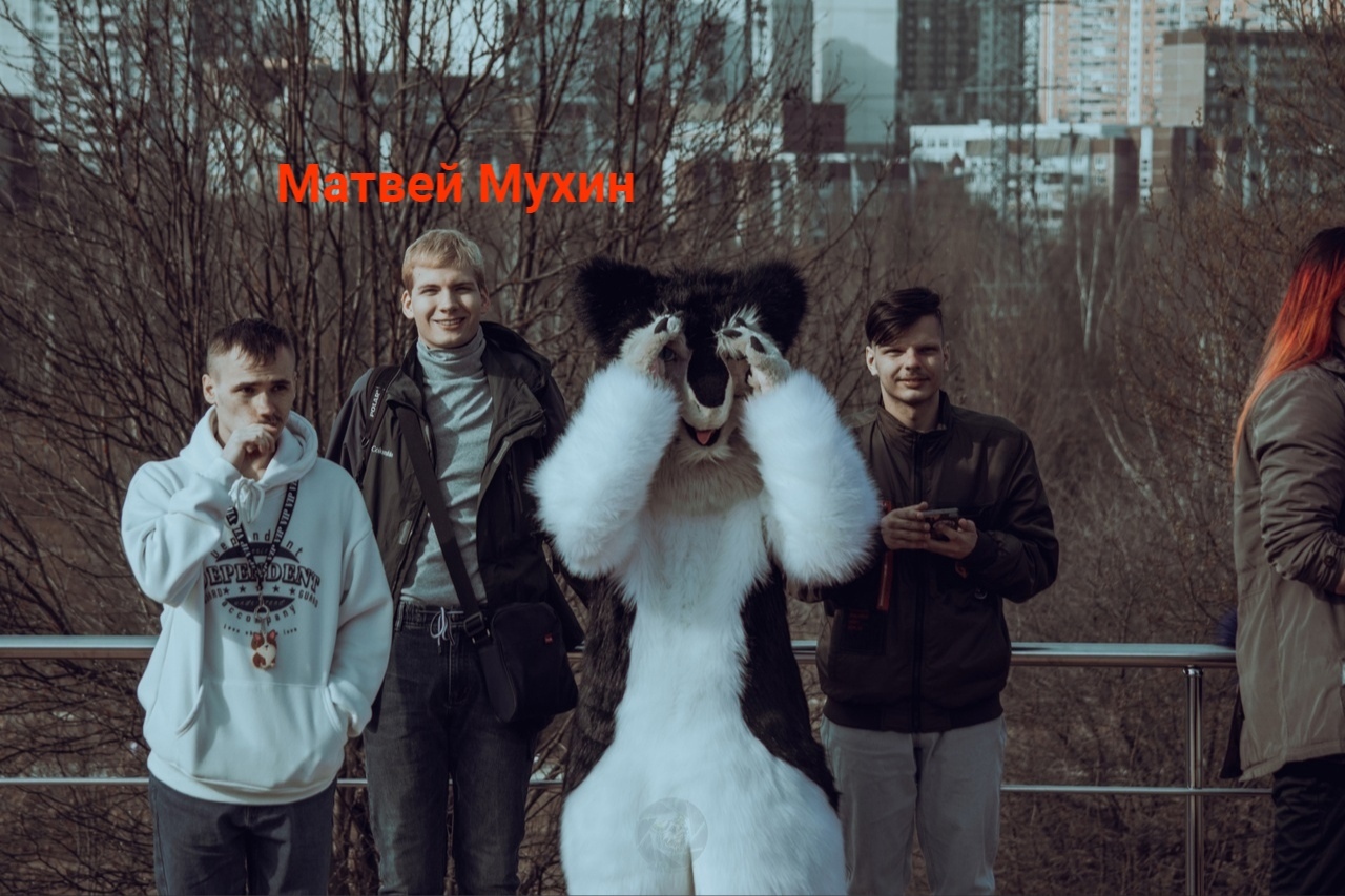 📋 Группа из четырёх человек на фоне городского пейзажа (высокий мост/набережная): подпись «Матвей Мухин» (красным); один из четырёх в белом фурсьюте-панде; кусты, многоэтажки вдали.