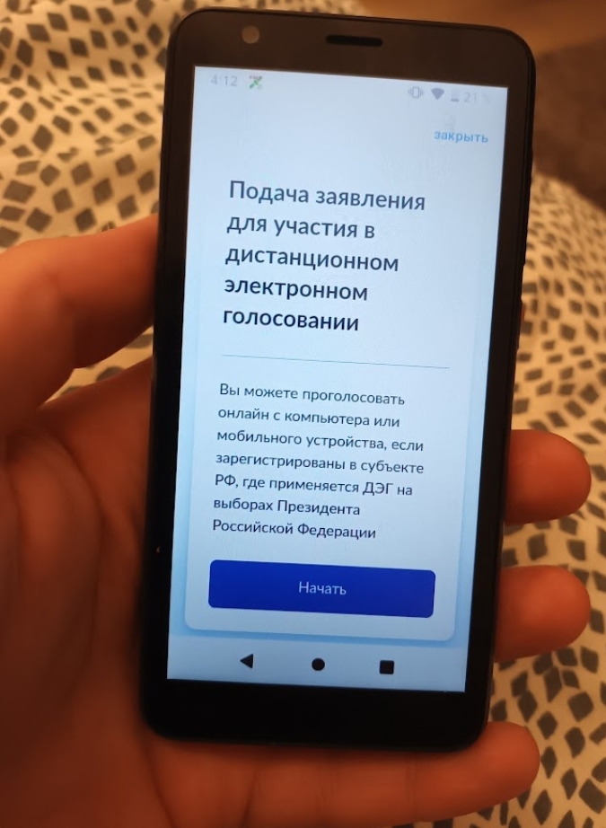 📷 Рука держит смартфон (4:12, значок местоположения, Wi-Fi); на экране: «Подача заявления для участия в дистанционном электронном голосовании. Вы можете проголосовать онлайн с компьютера или мобильного устройства, если зарегистрированы в субъекте РФ, где применяется ДЭГ на выборах Президента Российской Федерации»; синяя кнопка «Начать».