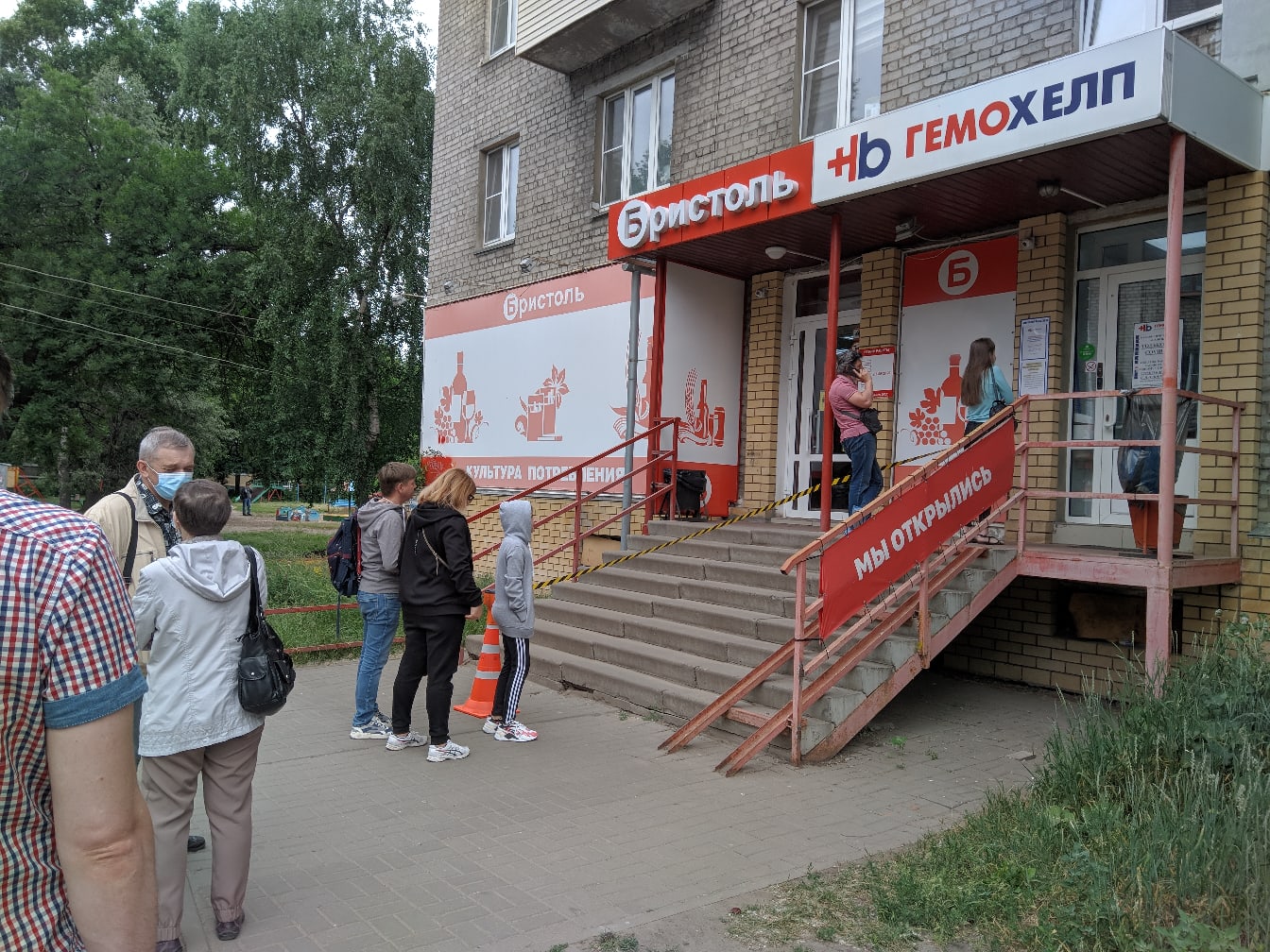 📷 Очередь людей в масках у входа в медицинский центр: вывески «Эристоль» и «Гемохелп», красная надпись «МЫ ОТКРЫЛИСЬ», пандус, летний день