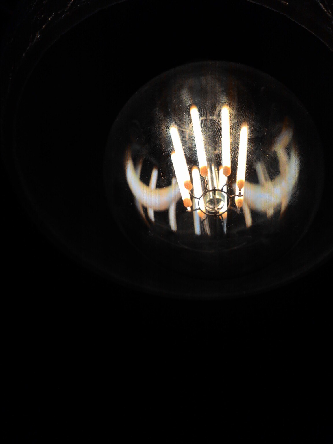 Фото снизу вверх, другой ракурс: та же LED-лампа Edison-стиля — светящиеся LED-нити хорошо видны сквозь прозрачную шарообразную колбу; оранжевые коннекторы; чёрный фон