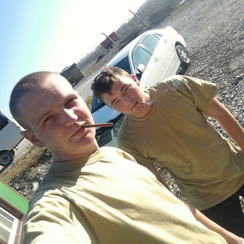 📷 Двое молодых мужчин в бежевых/военных футболках делают сэлфи у припаркованной машины на пустыре.