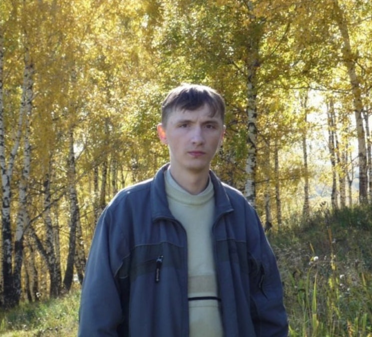 📷 Молодой человек в серо-голубой куртке стоит в берёзовом лесу с пожелтевшими листьями, смотрит в камеру.