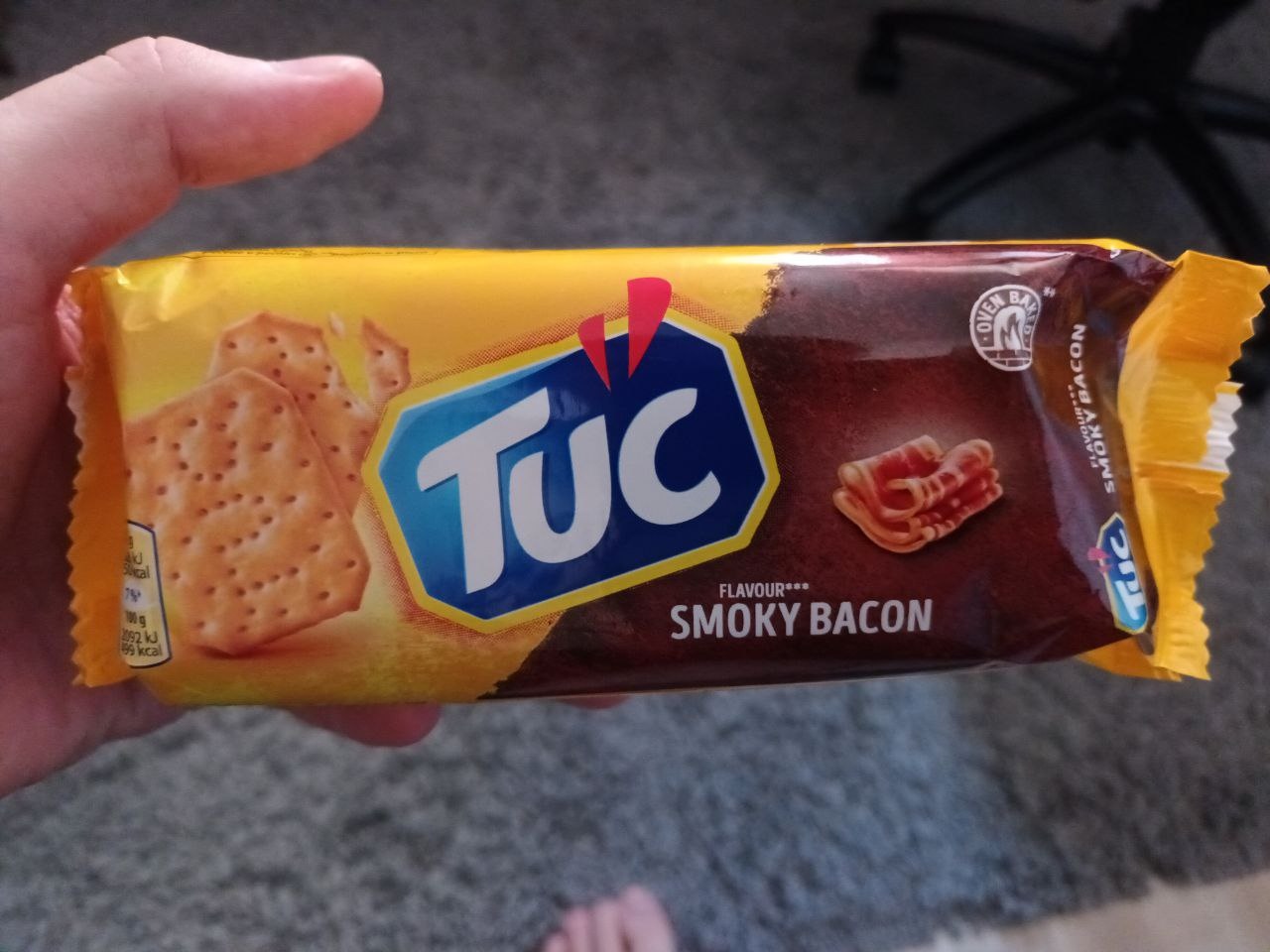 📷 Рука держит пачку крекеров TUC (жёлтая упаковка с коричневым): «FLAVOUR SMOKY BACON» (вкус копчёного бекона).