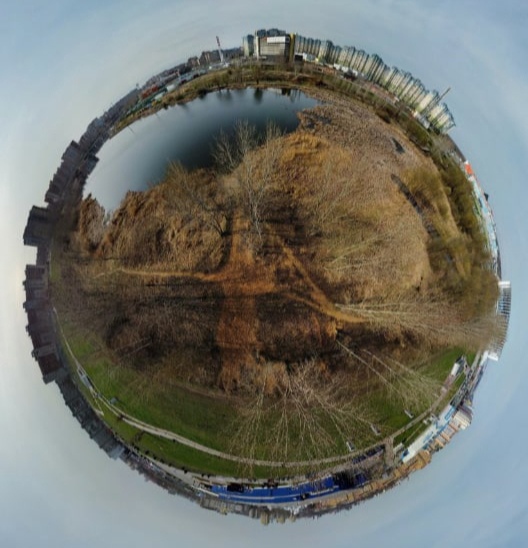 📷 «Крошечная планета» (стереографическая проекция): городская сцена — река или пруд, голые осенние деревья, жилые многоэтажки на заднем плане, дорога или рельсы; поздняя осень.