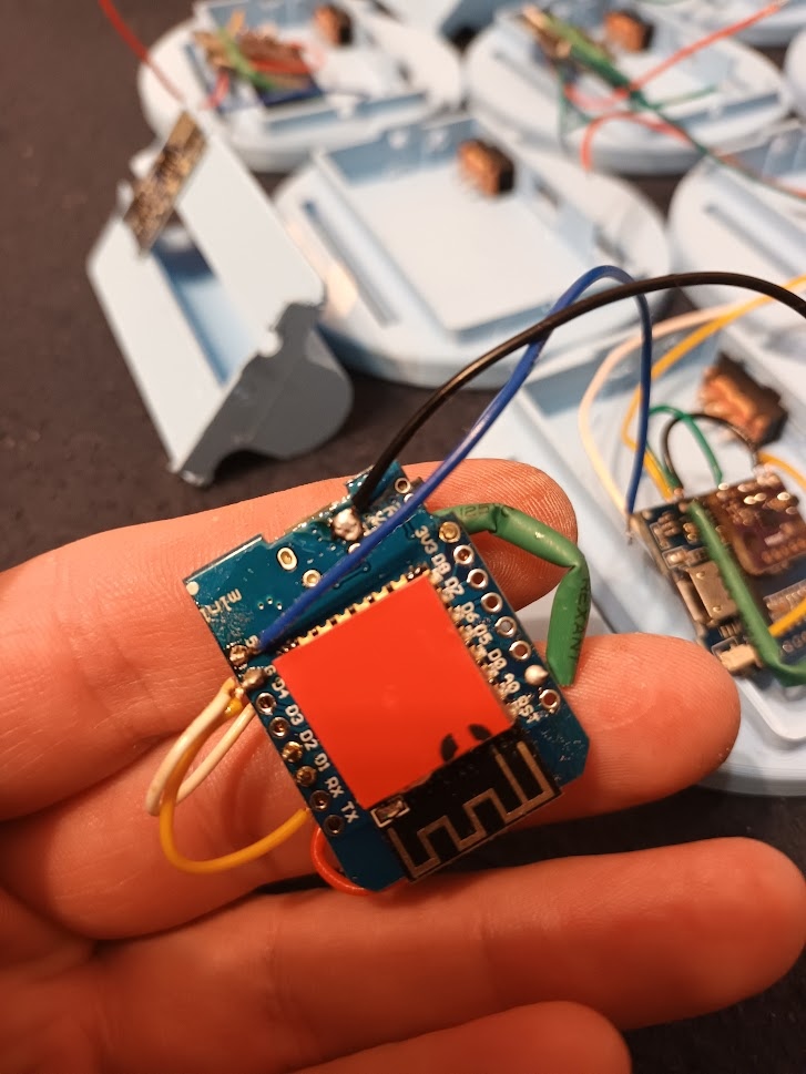 📷 На ладони — плата SlimeVR трекера: синяя PCB с красным WiFi-модулем (ESP8266), припаянные провода (жёлтый, синий, красный). На заднем плане — ещё корпуса и платы.